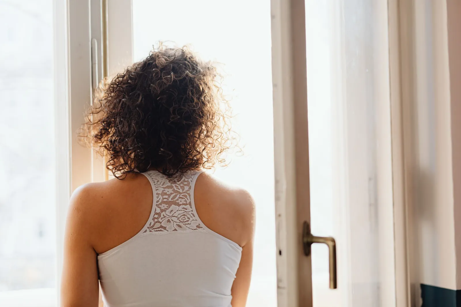 A woman looking out of an open window in soft morning light