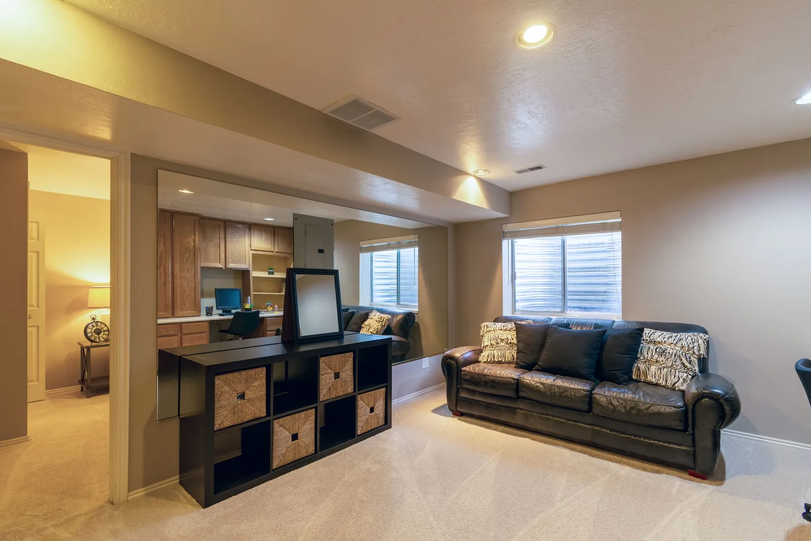 A finished basement family room with carpet, a leather sofa and a small office nook