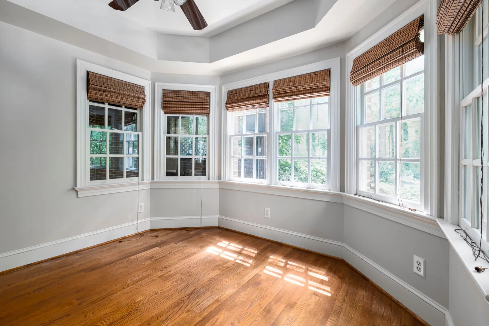 A bright, empty room with wood floors and sunlight coming through a bay of tall windows