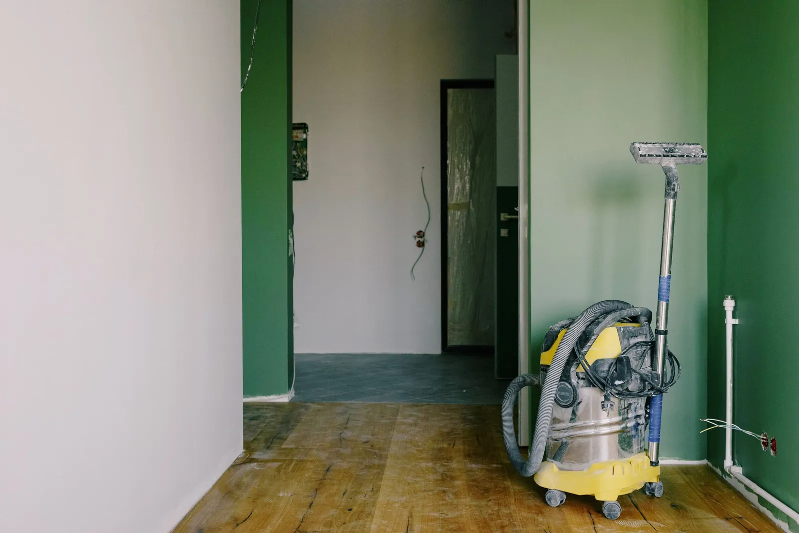 A wet-dry vacuum standing in an emptied hallway with bare wood floors