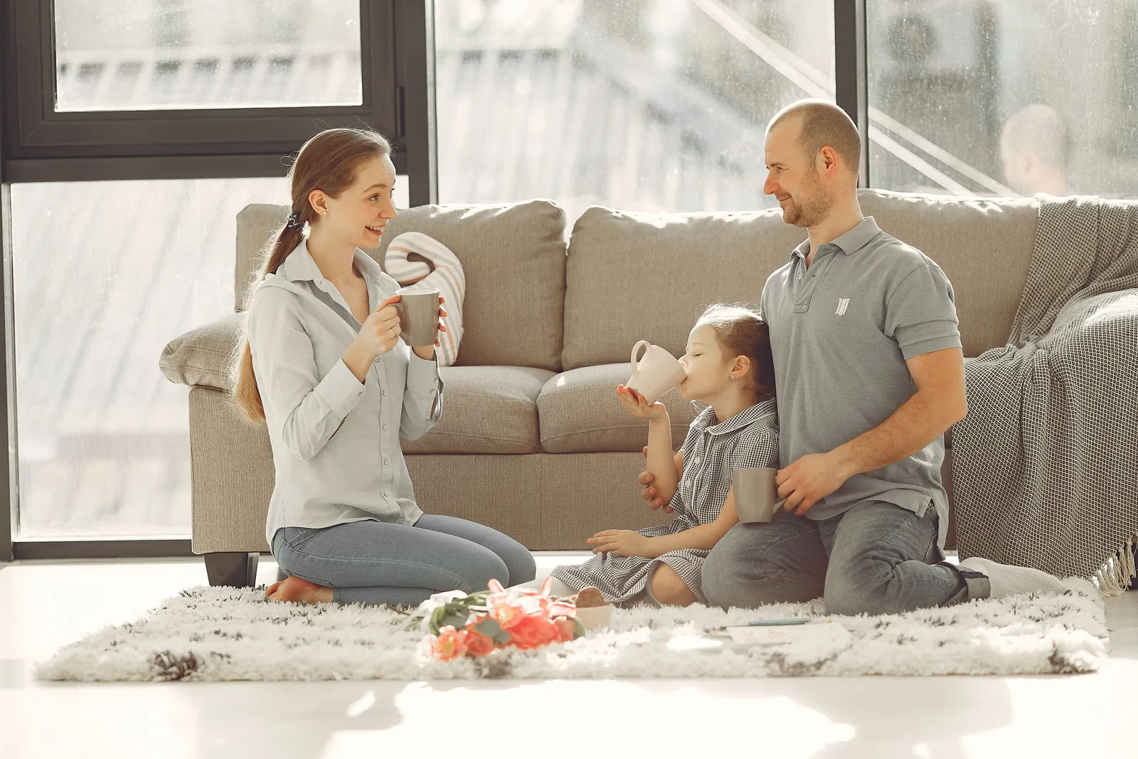 A family sharing drinks on a rug in a bright living room