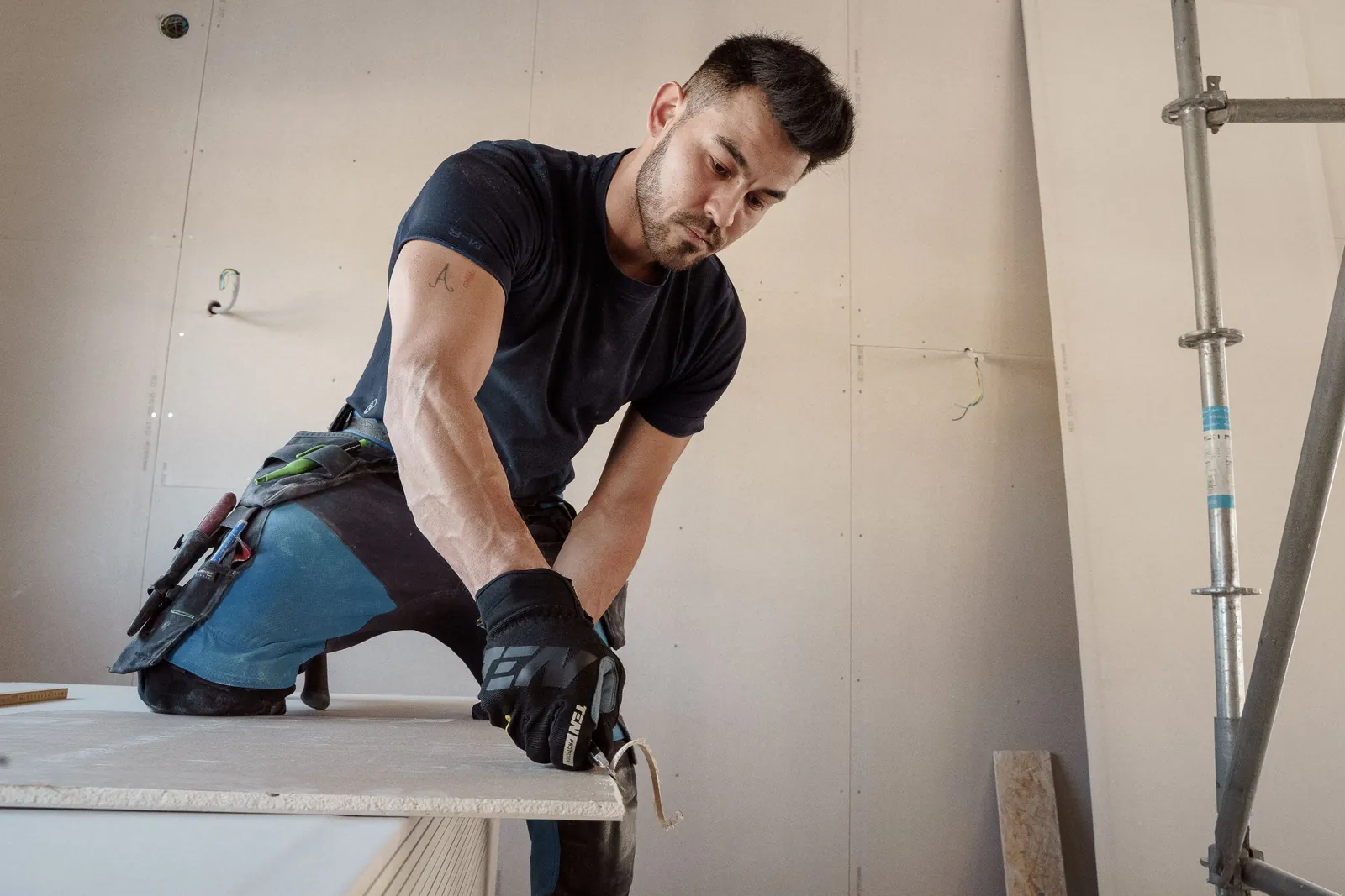 A tradesman in work gloves cutting a sheet of drywall in a room being rebuilt